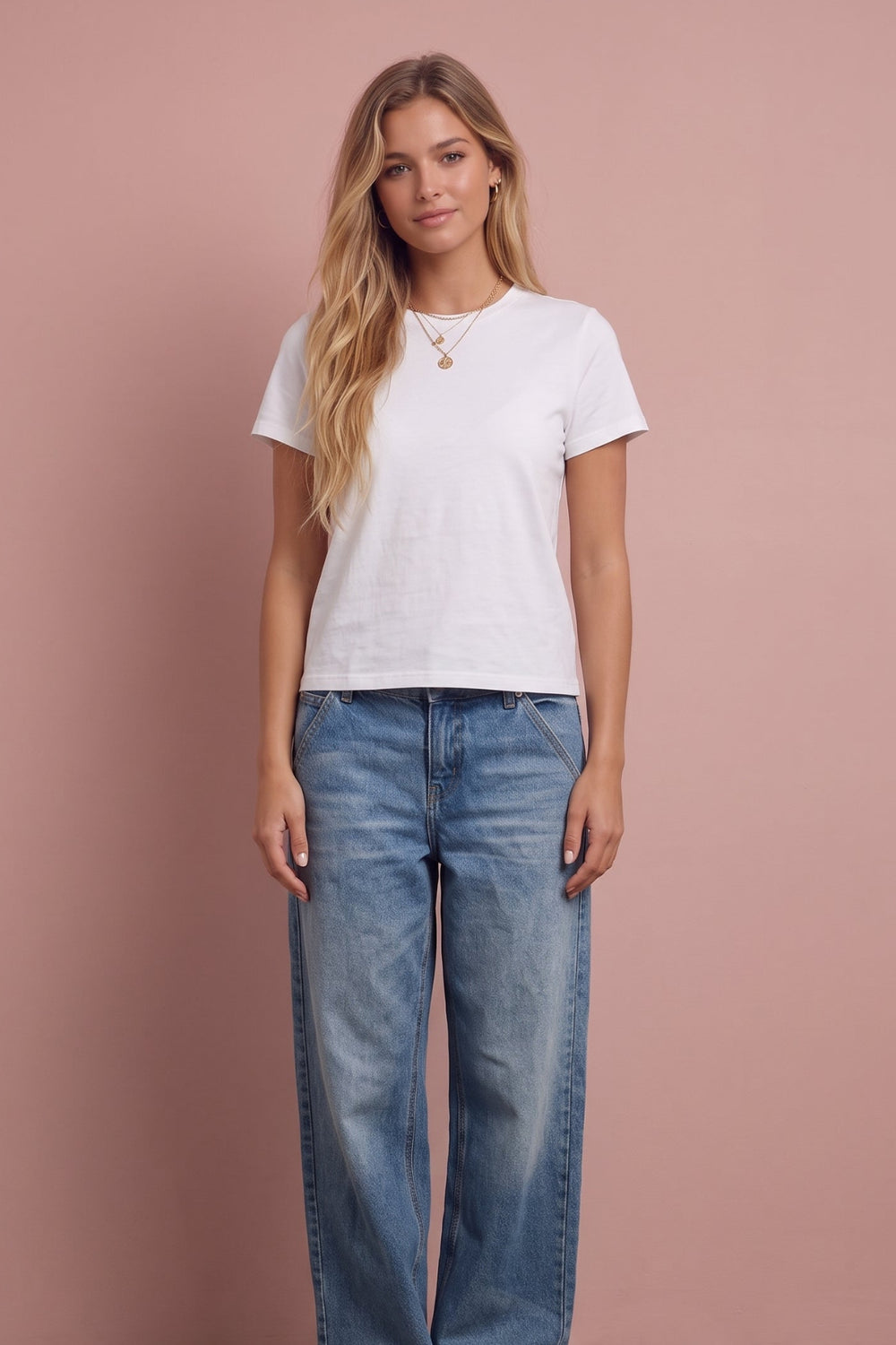 Woman wearing white short-sleeve cotton tee and blue jeans against pink background.