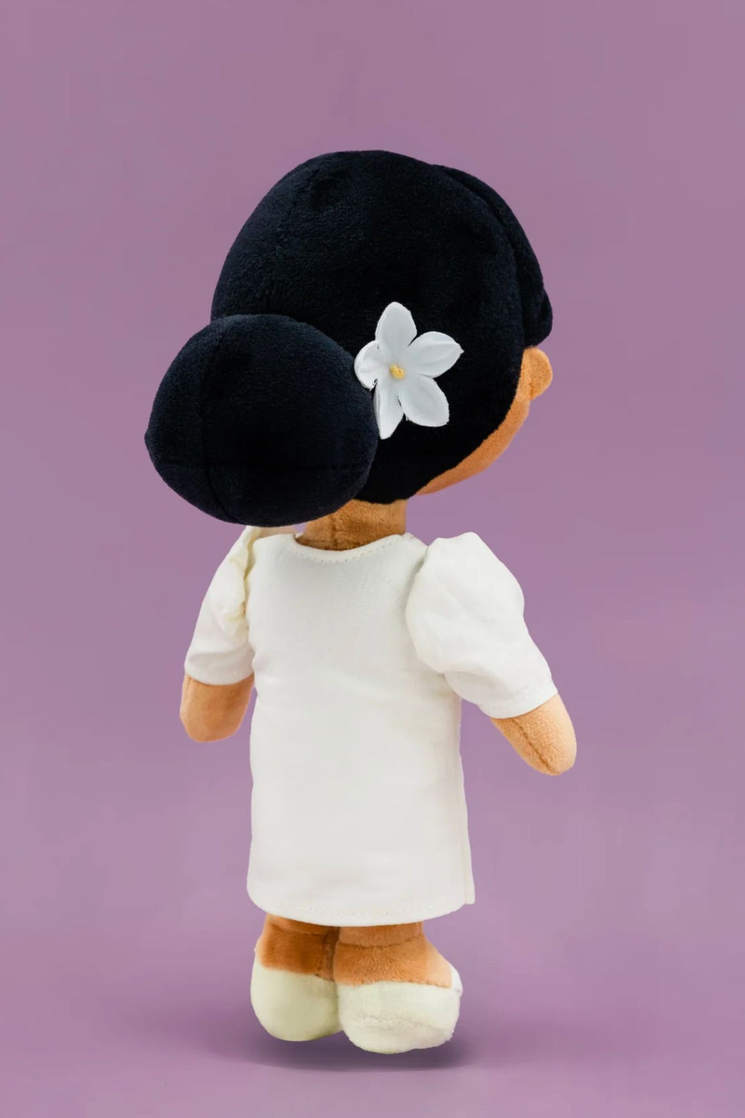 Plush penguin-shaped doll in traditional black hat, white flower decoration, and white outfit standing against purple background.