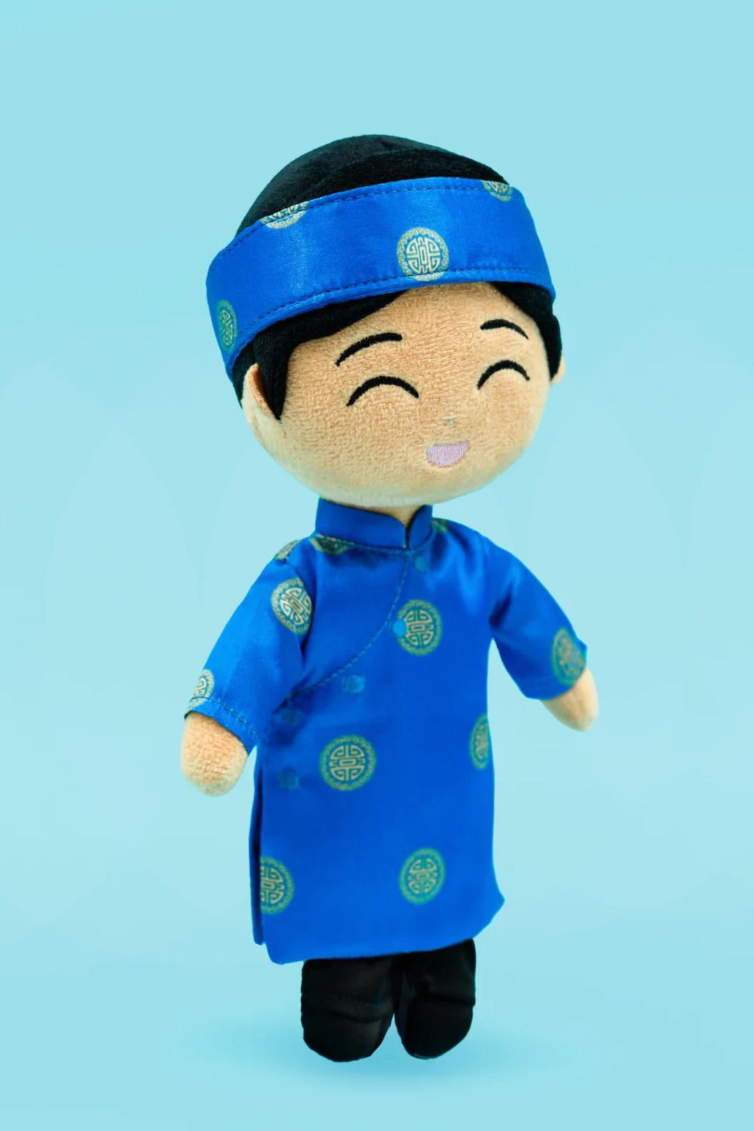 A smiling plush doll wearing a blue robe and headband with traditional Chinese designs, holding a friendly expression.