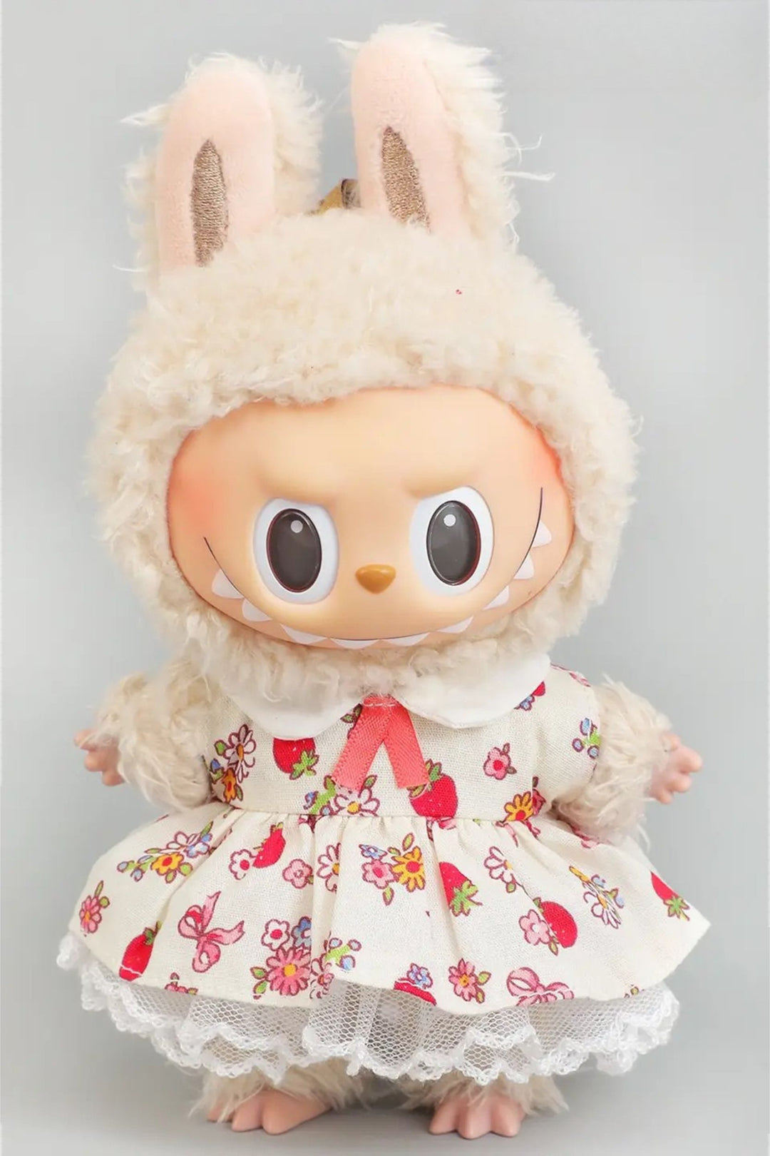 Labubu plush figure wearing a white dress with colorful flower and fruit print, large expressive eyes, and soft white fur accents.