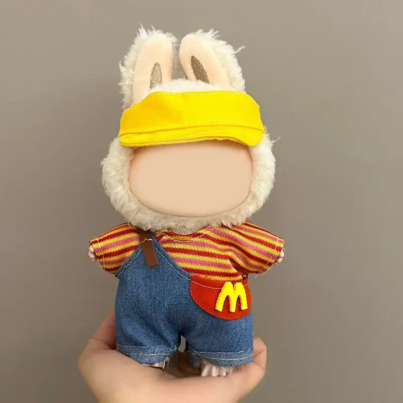 A plush toy wearing a yellow visor, striped shirt, and blue denim shorts, with a McDonald's logo on the shirt, representing the Labubu McDonald's uniform.