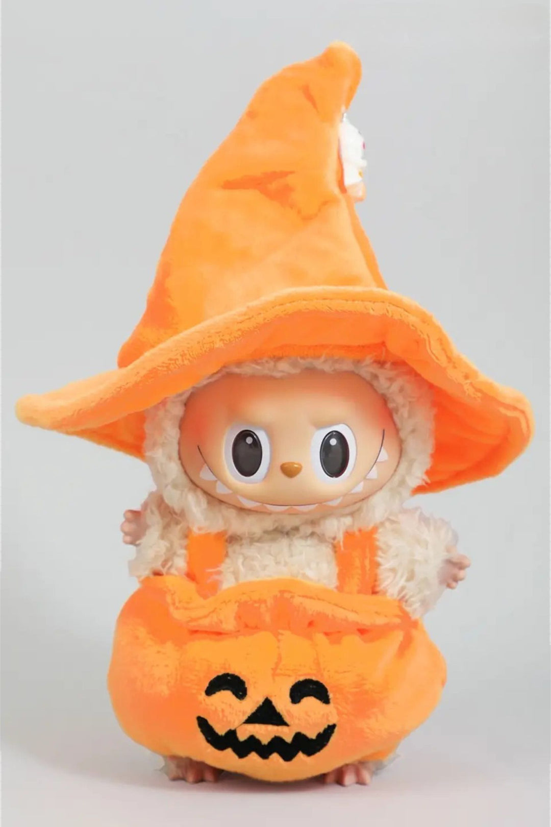 Plush toy in orange pumpkin costume with witch hat, big eyes, and smiling jack-o'-lantern face.