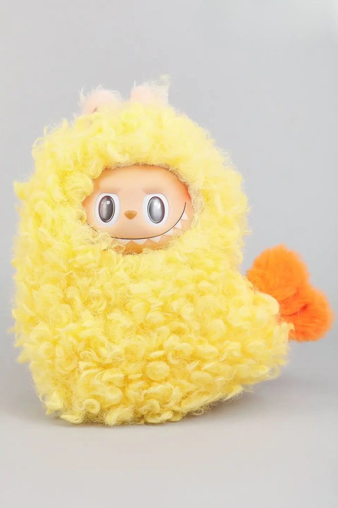 Yellow fluffy plush creature with big eyes and an orange pompom tail, wearing a textured yellow outfit resembling shrimp tempura.