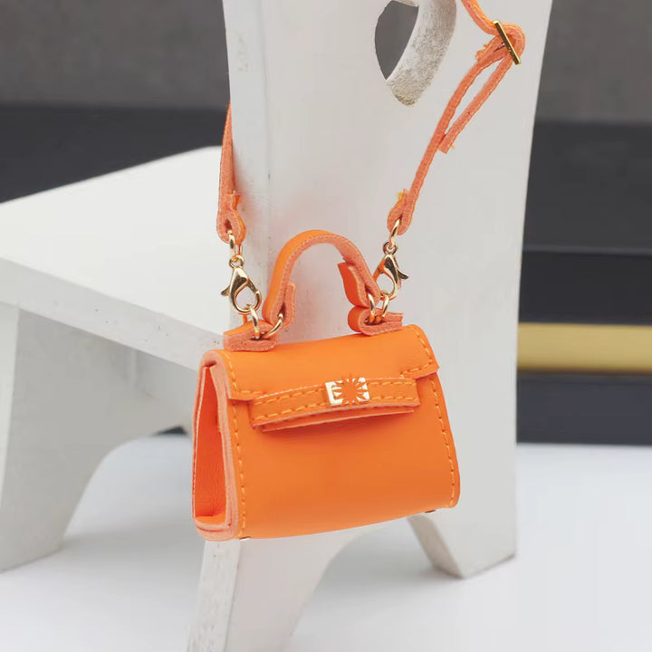 A vibrant orange handbag with a miniature handbag charm, featuring a sleek, stylish design and gold-tone hardware.
