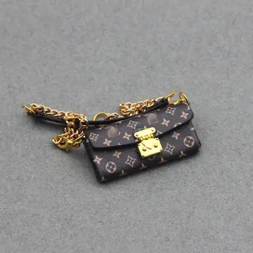 A small brown designer shoulder bag with a gold chain strap and a stylized decorative front panel.