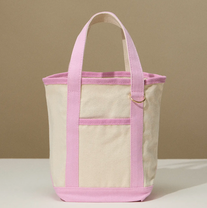 Beige canvas tote bag with pale pink handles and trim, featuring a spacious interior and a simple, classic design.