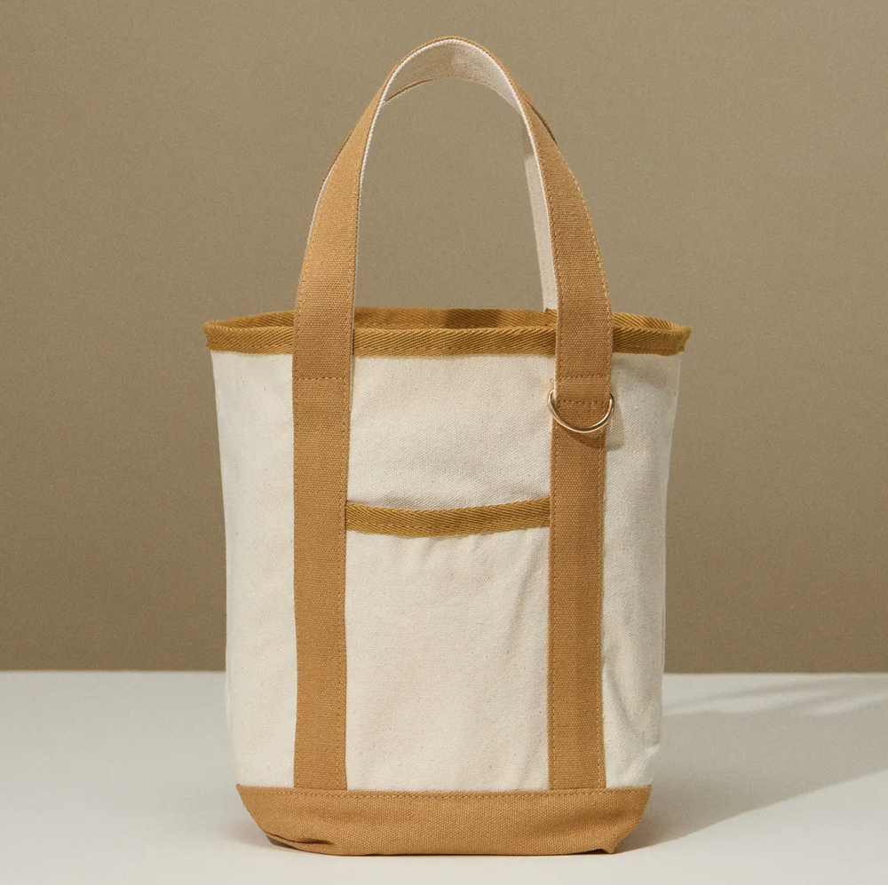 A small, rectangular canvas tote bag in a natural beige color with tan handles and trim, featuring a simple, minimalist design.