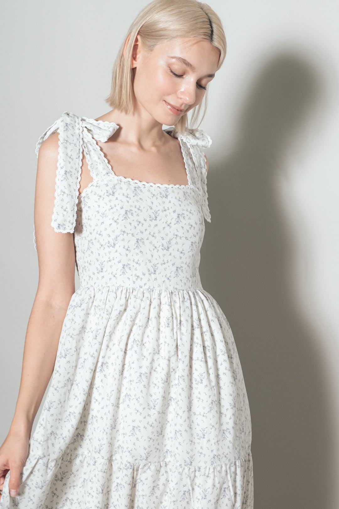 Woman wearing a white floral dress with bow straps against a plain background