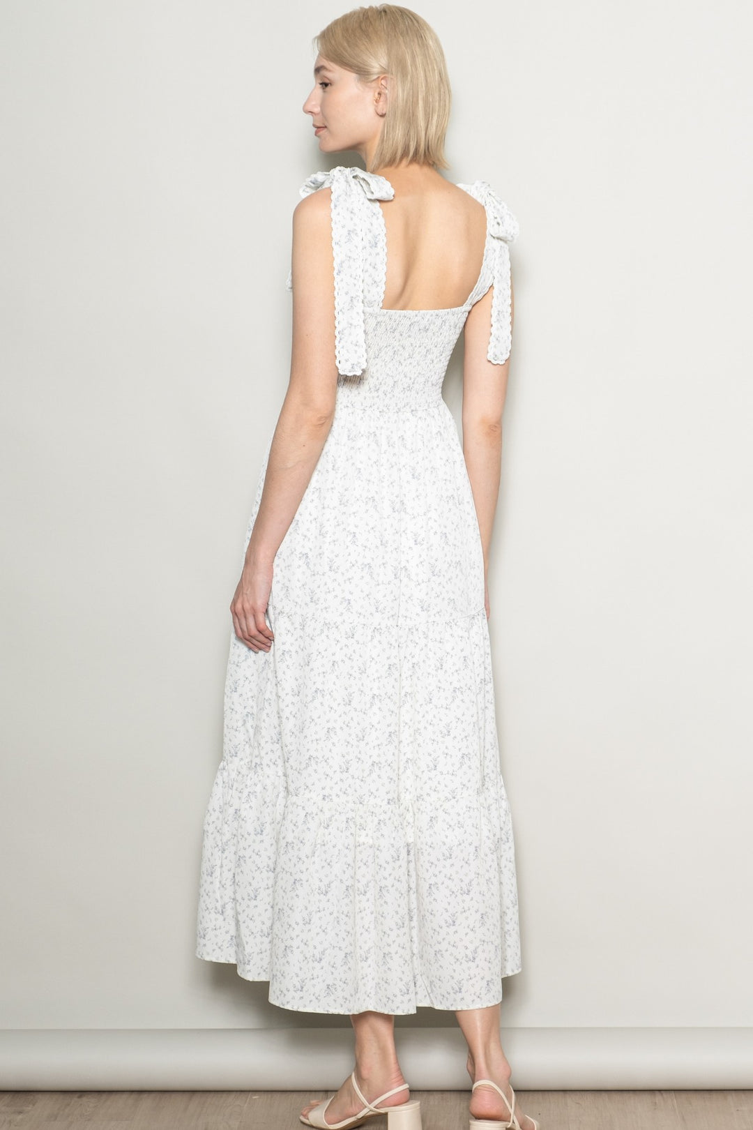 Woman wearing a white dress with floral pattern against a plain background