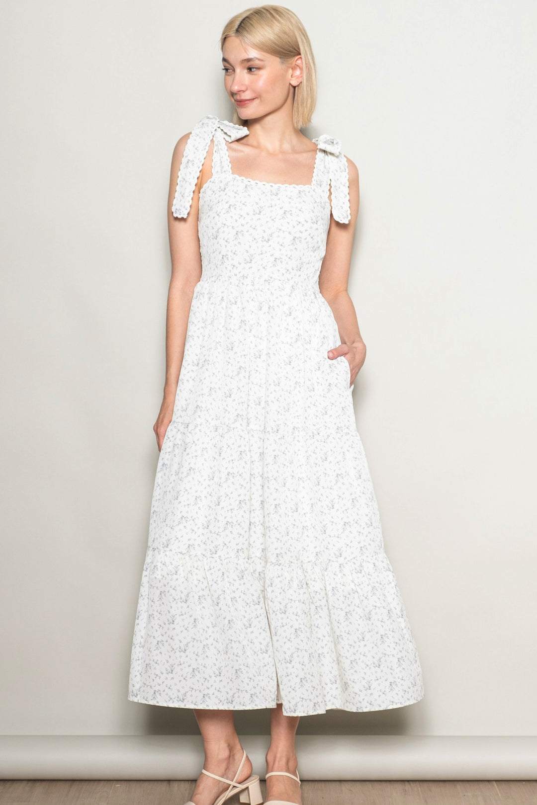 Woman wearing a white dress with floral pattern against a plain background