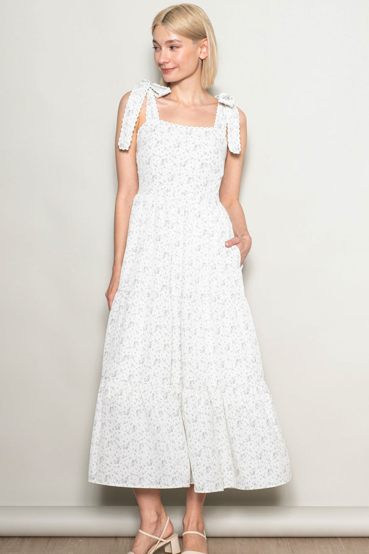 Woman wearing a white dress with floral pattern against a plain background