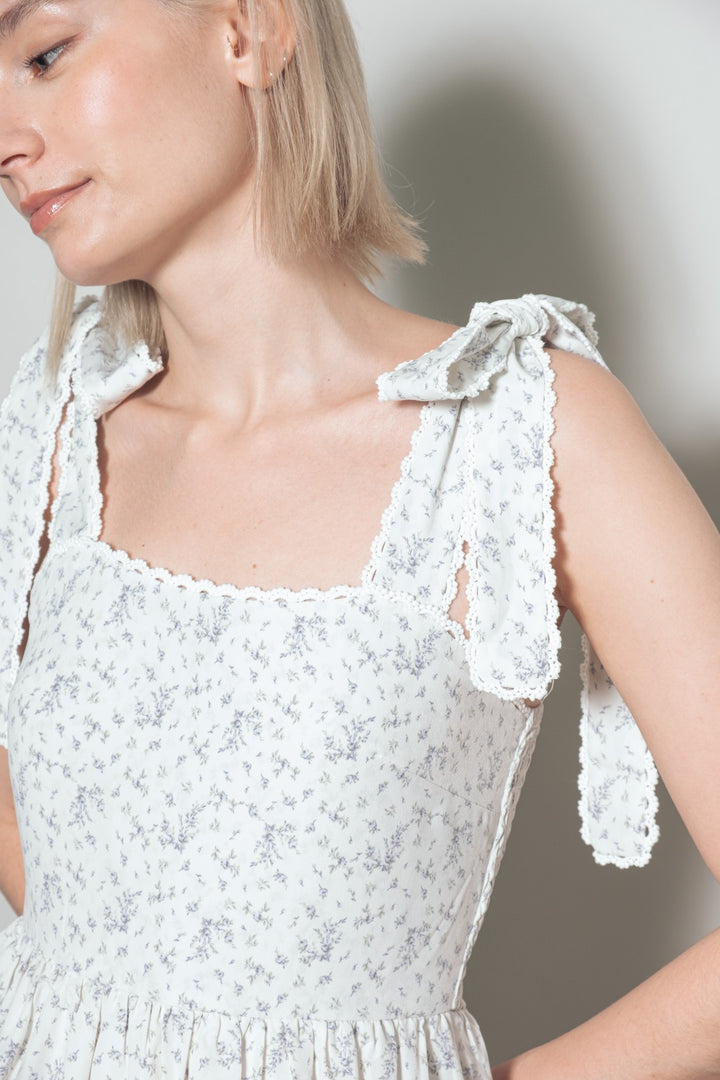 White floral dress with bow straps worn by a model against a neutral background