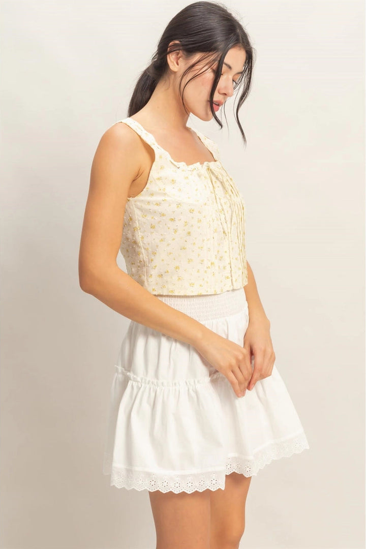 A young woman wearing a white crop top with a delicate floral print, paired with a white skirt with eyelet trim.