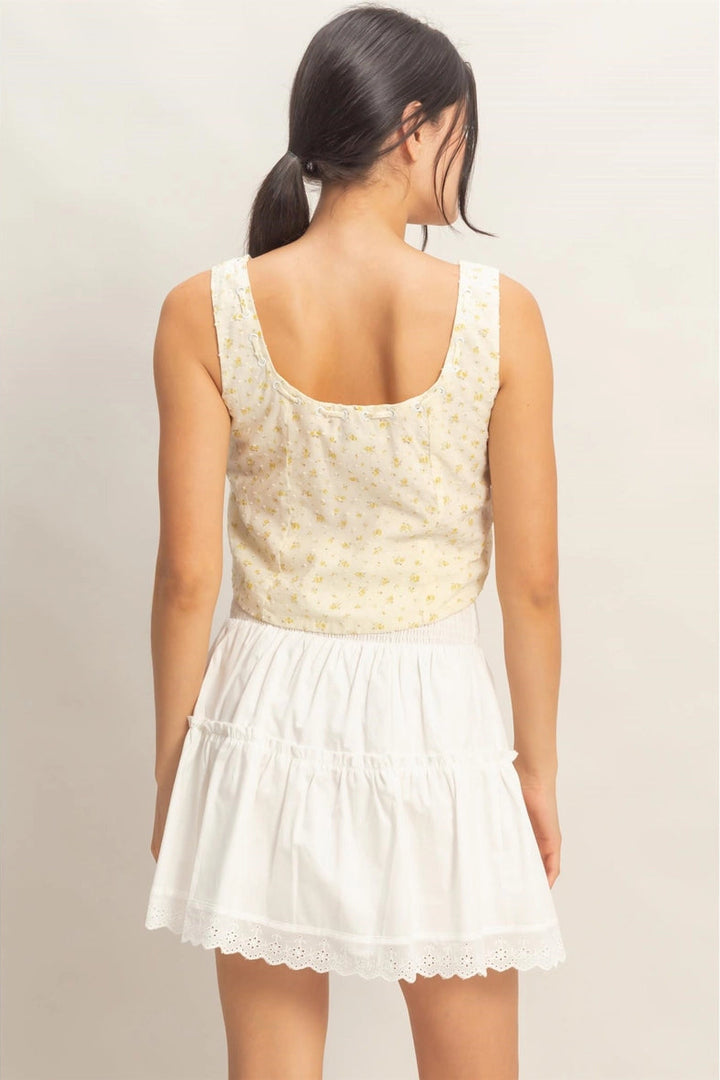 A light-colored crop top with a floral print, featuring a scoop neckline and a relaxed fit. The image shows the back view of the top on a model with long dark hair.