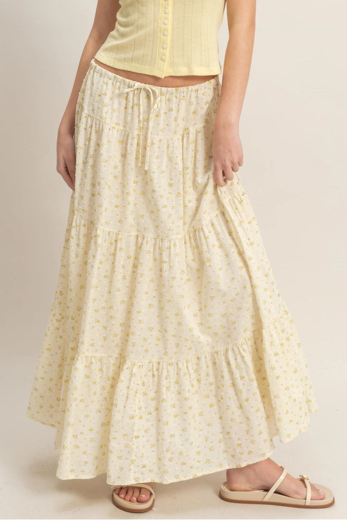 A feminine, floral tiered skirt with a high-waisted, ruffled silhouette in a light, off-white background.