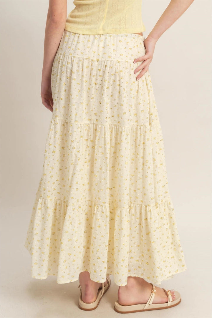 A flowing, yellow floral-patterned maxi skirt with a tiered, ruffled design and an elastic waistband.