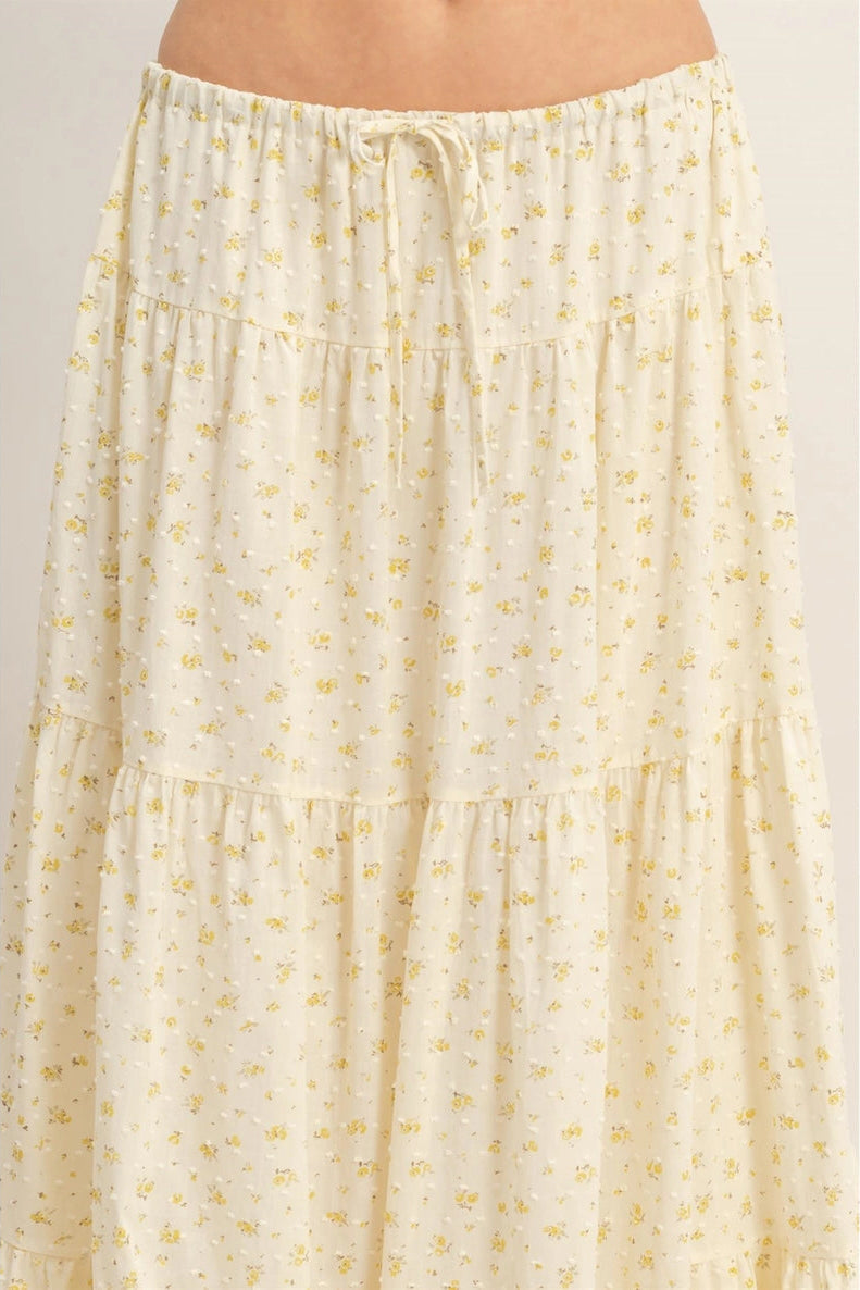 A soft, flowing ivory-colored skirt with a delicate floral print, featuring a tiered, ruffled silhouette and a drawstring waist.