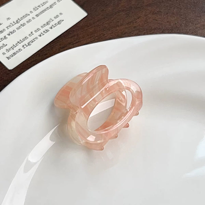 A soft pink, oval-shaped hair claw clip made of transparent plastic material with a textured, scalloped edge design.