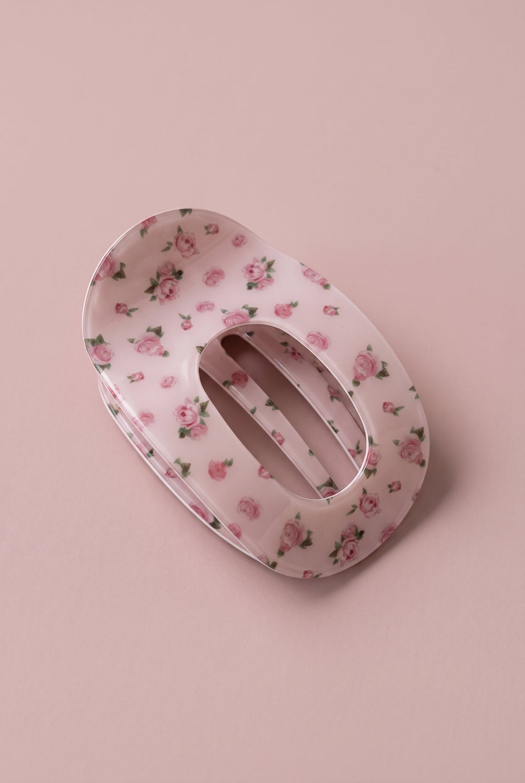A pink hair claw clip with a delicate pink and green floral pattern, shown on a solid pink background.
