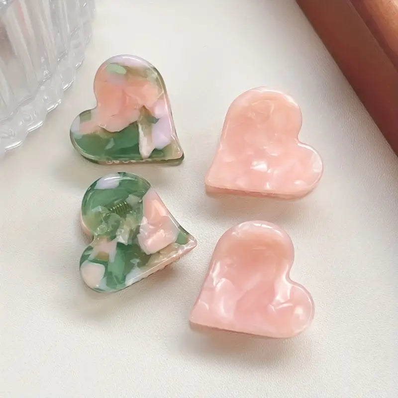 Heart-shaped resin claw clips in pink and green camouflage patterns, approximately 0.75 inches in size.