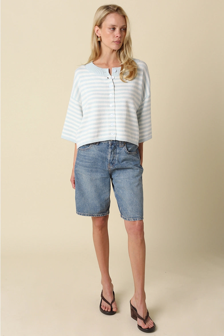 A loose, knit top in a white and light blue striped pattern, with a buttoned neckline and three-quarter length sleeves, worn by a woman with long, blonde hair.