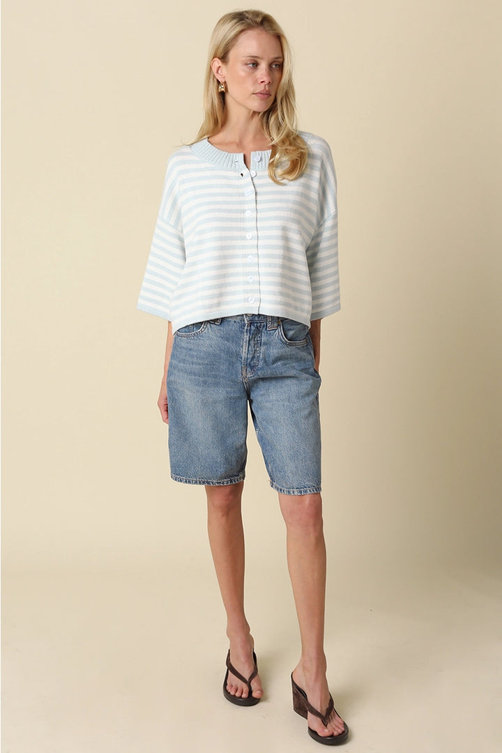 A loose, knit top in a white and light blue striped pattern, with a buttoned neckline and three-quarter length sleeves, worn by a woman with long, blonde hair.