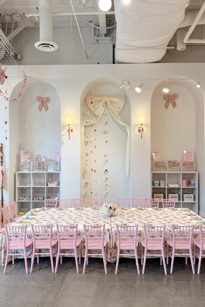 Pink and white themed party venue with floral decor, Chiavari chairs, and tables set for a special event.
