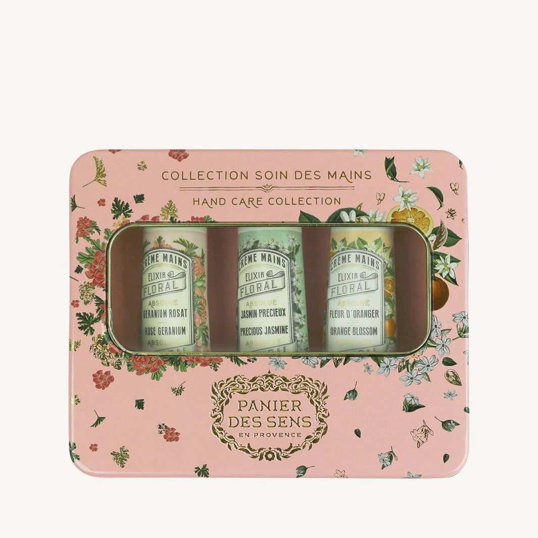 A metal gift tin with a floral pattern in soft pink, green, and gold, containing three hand cream absolutes in rose geranium, precious jasmine, and orange blossom scents.