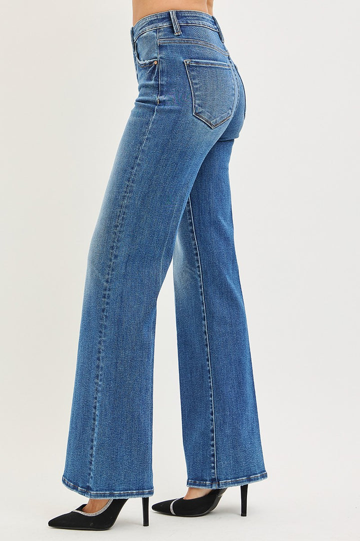 High-rise wide flare jeans in medium blue denim with tummy control feature, showcasing model's slim figure and stylish pointed-toe black heels.
