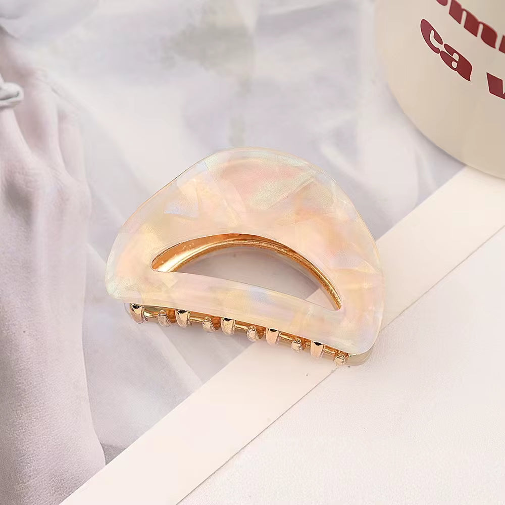 A semi-circular hair claw clip made of translucent beige material with a gold-toned metallic accent along the top edge.