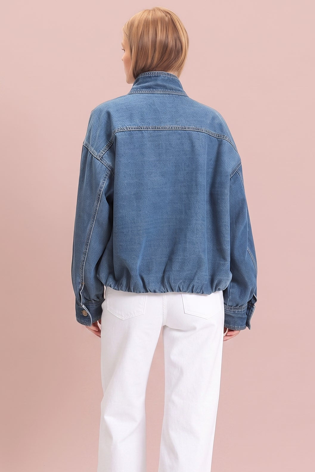 A model shown from the back wearing a blue denim jacket and white wide-leg trousers, standing against a solid dusty pink background.