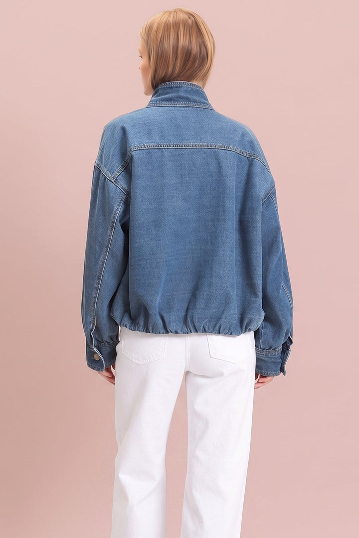 A model shown from the back wearing a blue denim jacket and white wide-leg trousers, standing against a solid dusty pink background.