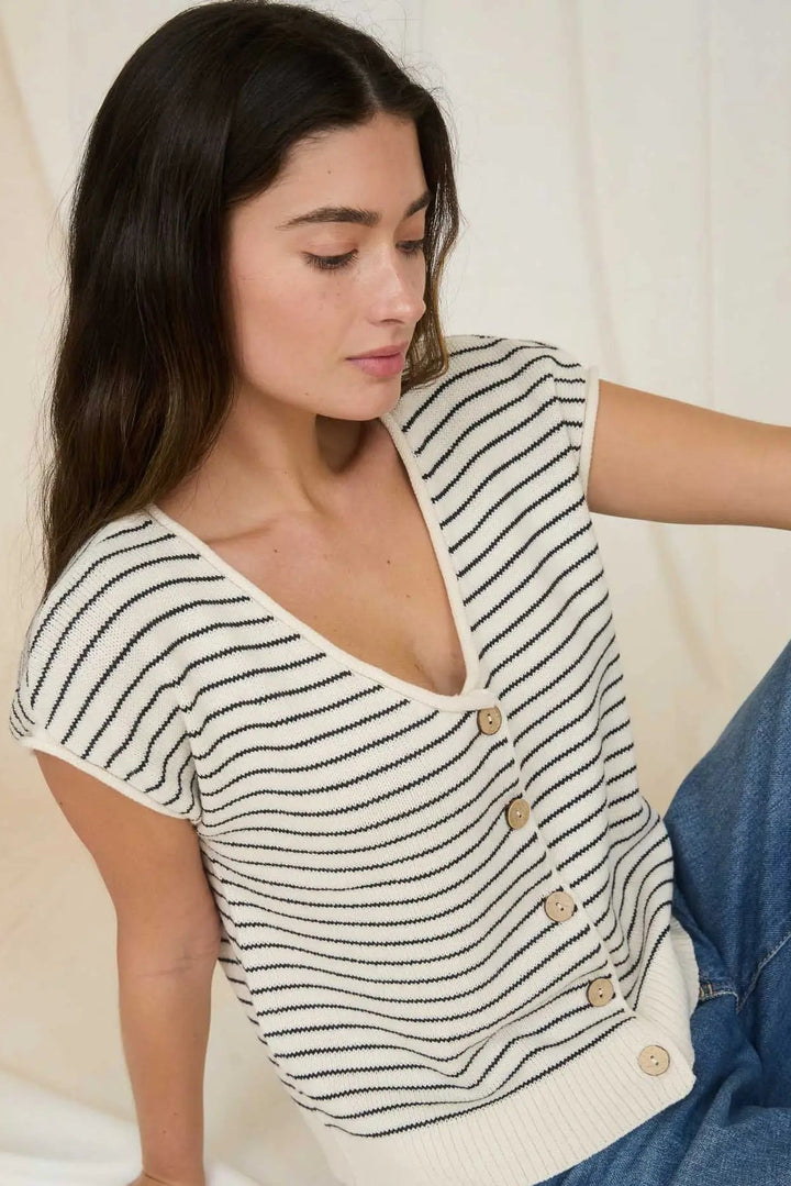 Woman wearing a striped top with buttons and jeans on a neutral background