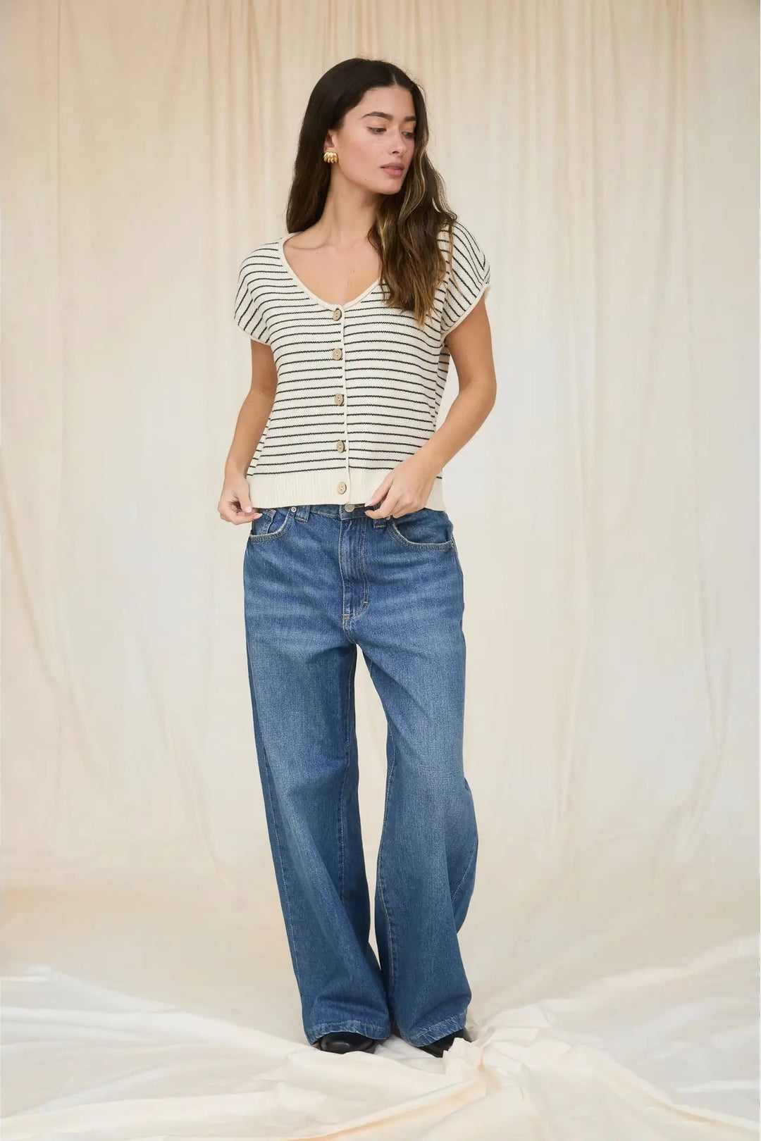 Woman wearing a striped shirt and blue jeans against a plain background