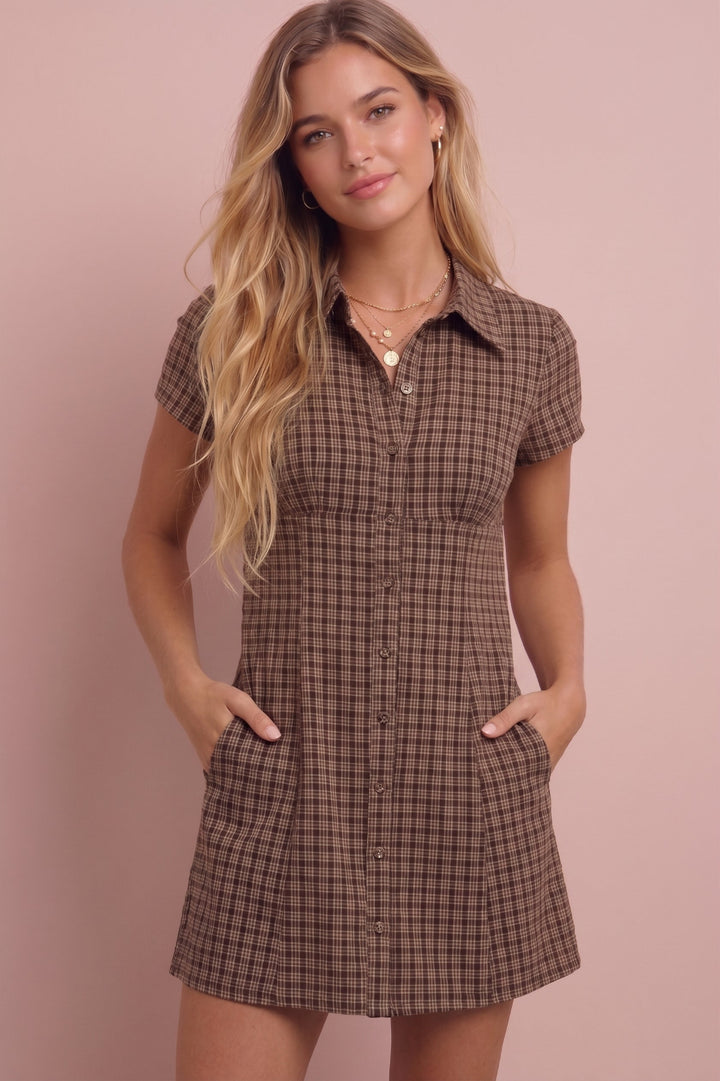 Brown plaid short-sleeve button-front mini dress on model against pink background.