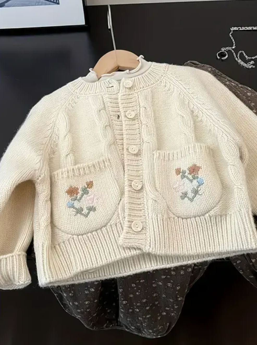 Cream-colored knit cardigan with floral embroidery and cable-knit texture, designed for kids.