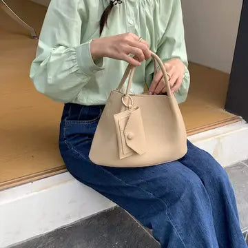A soft, beige microfiber leather crossbody tote bag with a compact, structured silhouette and a detachable shoulder strap.