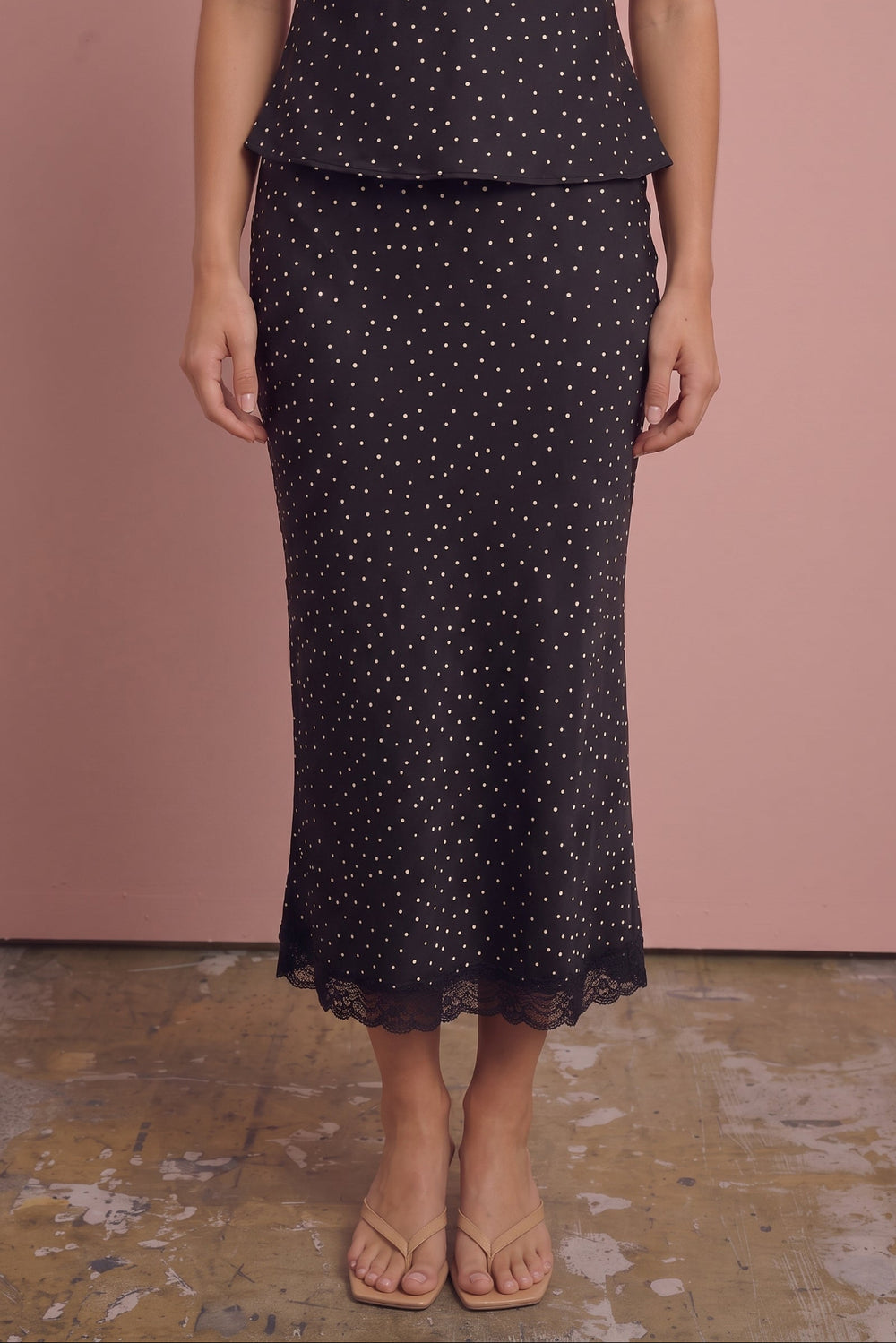 Black polka dot satin skirt with lace hem, worn with nude sandals, front view.