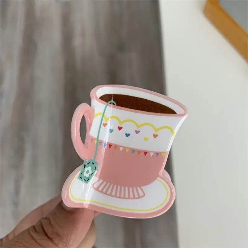 A whimsical pink teacup-shaped hair claw clip with colorful heart and banner designs, adding a playful touch to any hairstyle.