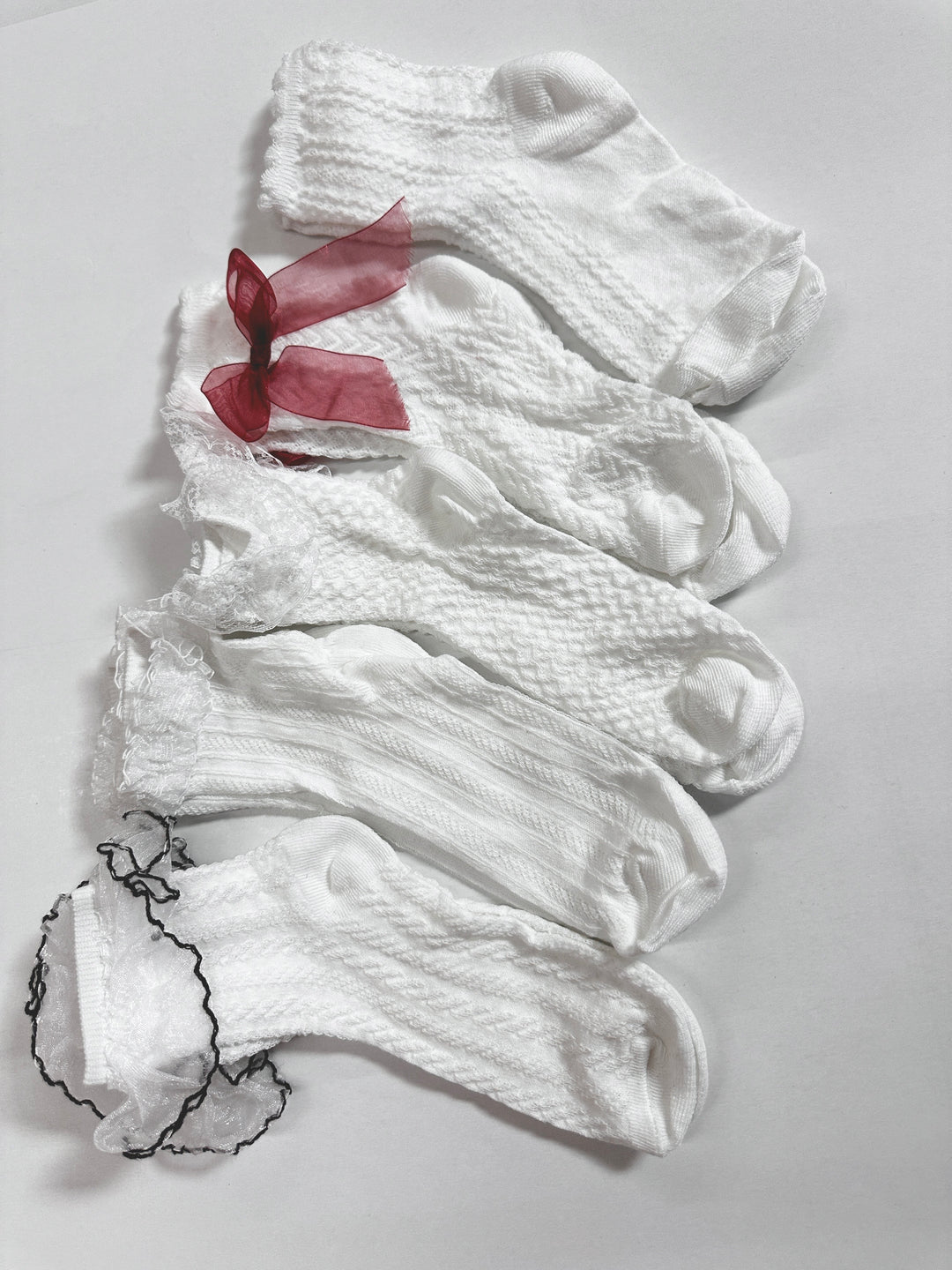 White textured children's socks with red ribbon accents, sold individually.