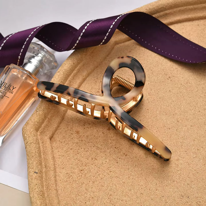 A purple ribbon-patterned tortoiseshell hair claw clip with a gold-tone metal accent.