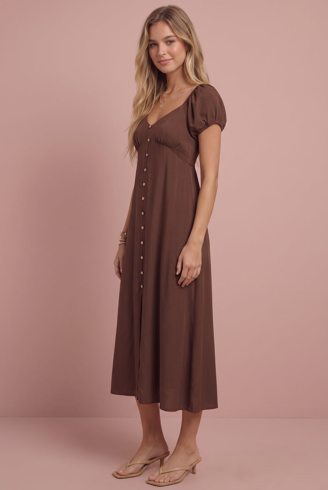 Brown smocked midi dress with short puffed sleeves and button front, modeled on pink background.