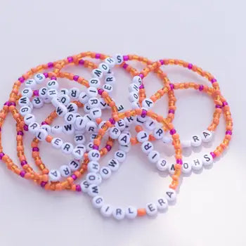 Colorful stretchy bracelets with pink, orange, and white beads spelling out "GIRL GANG" and "SHOWGIRL".