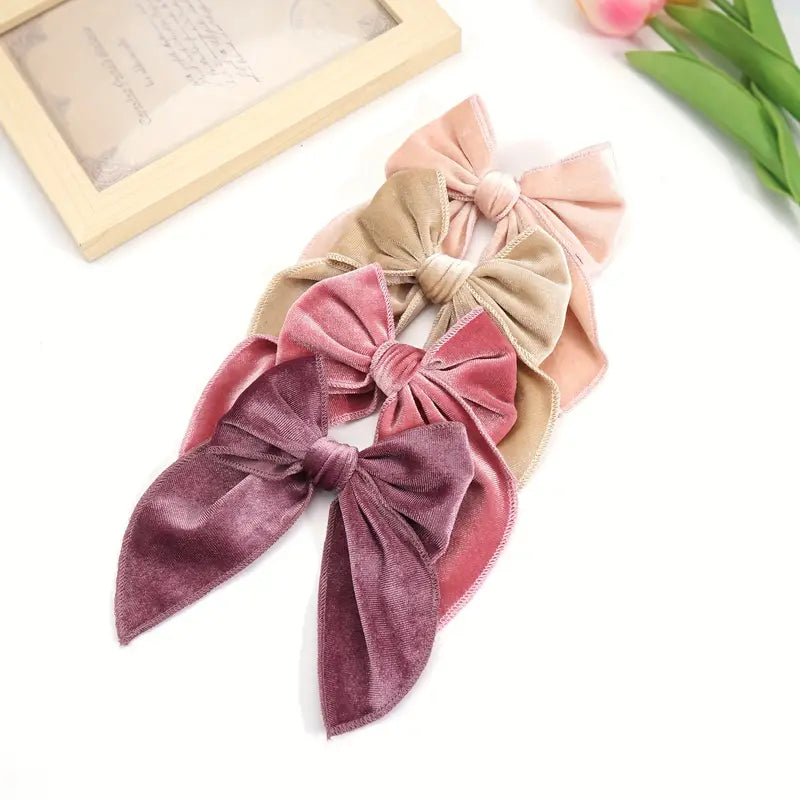 Assorted velvet hair bows in soft pink and neutral tones, with intricate knotted and looped designs, showcased against a pink tulip and wood-framed paper background.