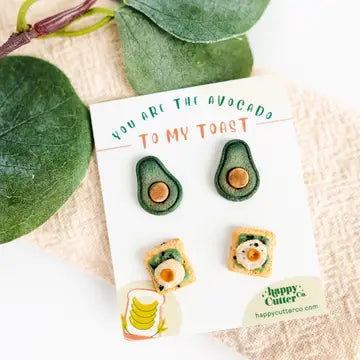 Colorful stud earrings featuring avocado and banana slice designs on green background.