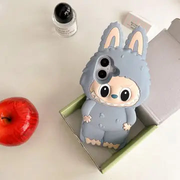 Gray plush rabbit phone case with large eyes and ears, sitting on a platform with an apple and a bottle.