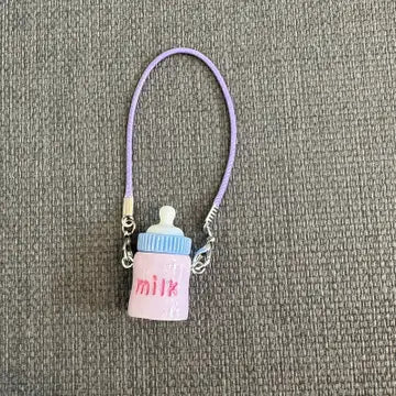 Small baby bottle charm in pastel pink and blue colors, dangling from a purple cord.