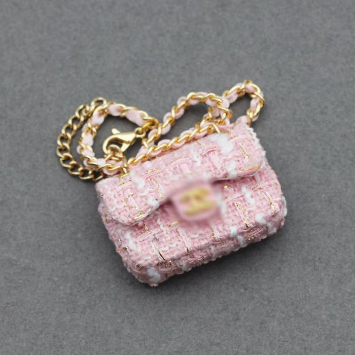 A miniature pink tweed shoulder bag with a gold chain strap and clasp, a unique designer handbag accessory.