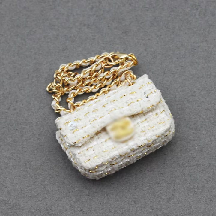 A small, handmade white and gold clutch bag with a delicate textured pattern and a long gold chain strap.