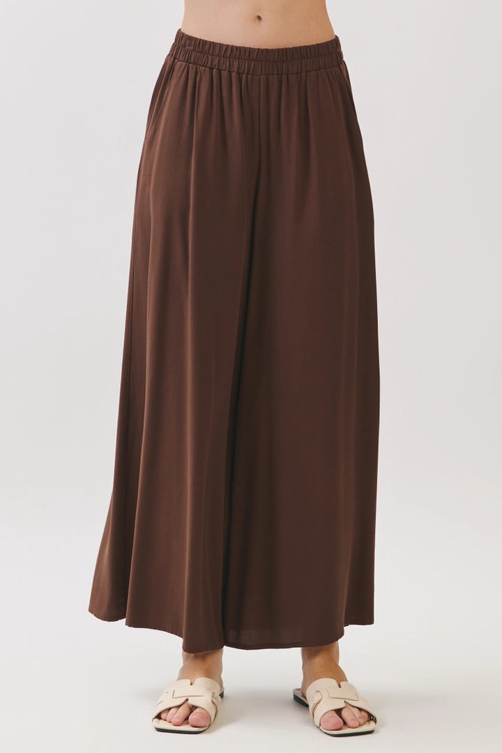 Brown wide leg pants with elastic waistband, full-length view on model wearing cream sandals.